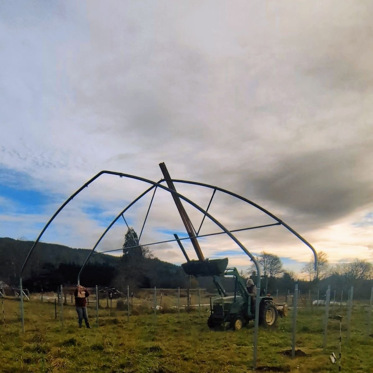 a tractor lifting trusses in the air to assemble a hoophouse