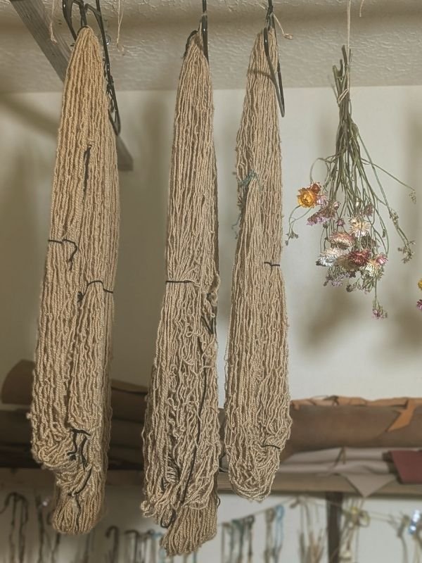 coffee dyed sheins of yarn hanging in a craft workshop with dried flowers