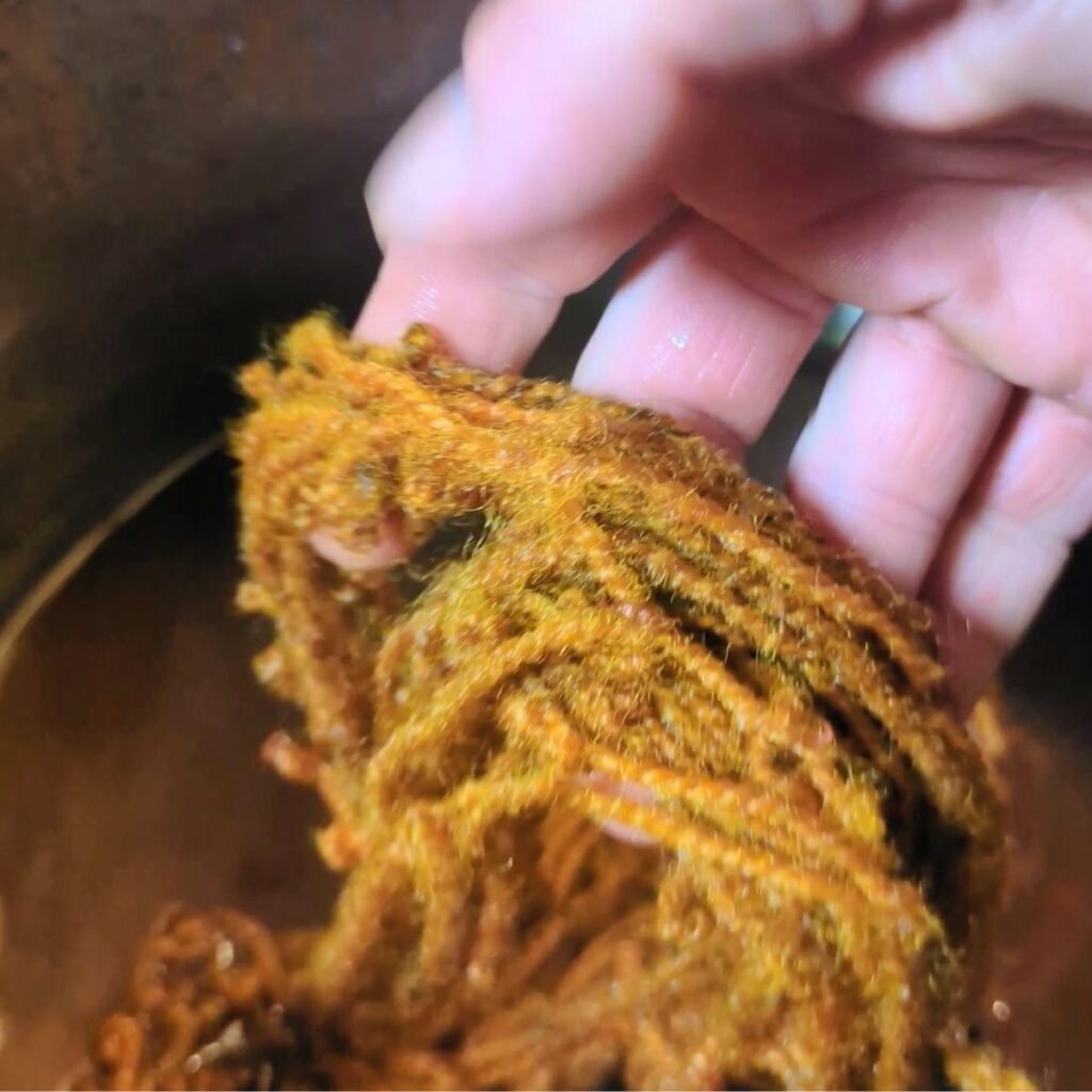 Wool yarn being dipped into a pot of natural dye to turn golden in color
