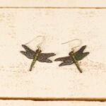 large leather dragonfly earrings displayed on a rustic wooden surface