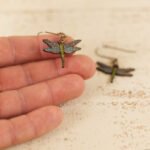 small leather dragonfly earrings held by a hand to show scale