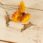 leather hummingbird dangle earrings displayed on a rustic wood surface with dried flowers