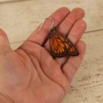 large leather monarch butterfly dangle earring held by a hand to show scale