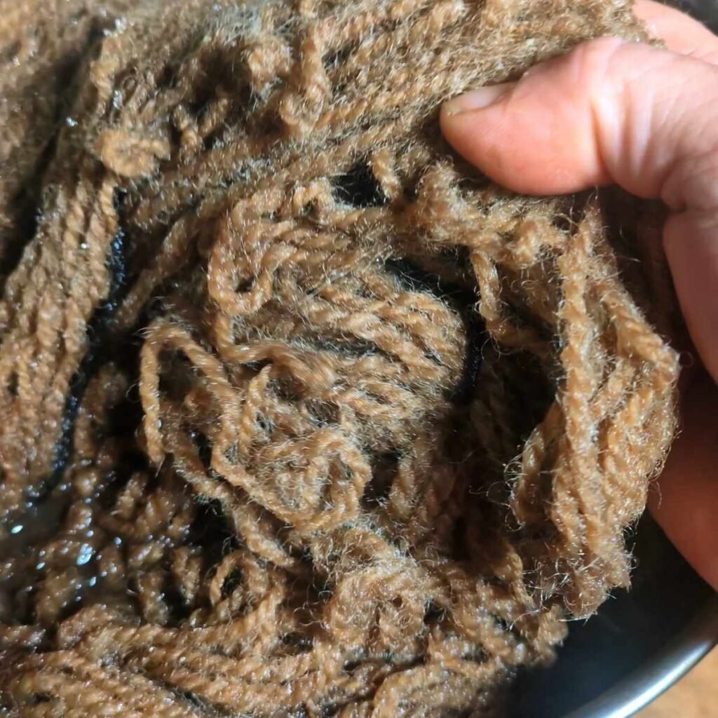 a hand pulling coffee dyed yarn out of a dye pot to illustrate the dye color