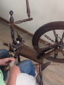 a person spinning wool into yarn on an antique spinning wheel