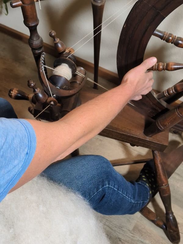 a person spinning on an antique spinning wheel